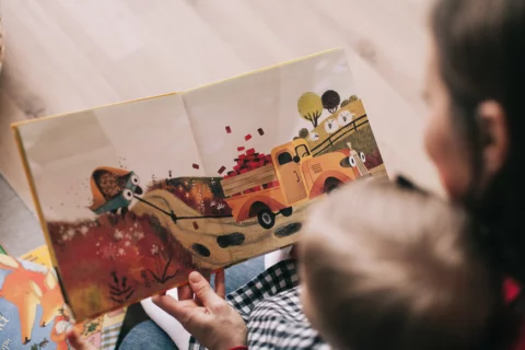 Photograph of mother holding her child in the foreground with a children's picture book in focus in the background. 