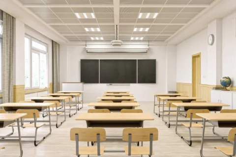 Photograph of a empty classroom with a screen in the front and student desks in a grid in the foreground.