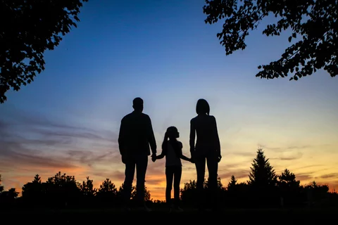 Photograph of a family standing amongst the trees silhouetted against the sunset.