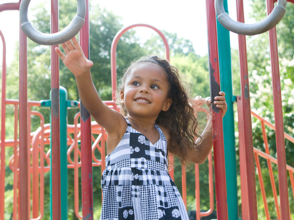 Photograph of young, black girl playing on a park playground.