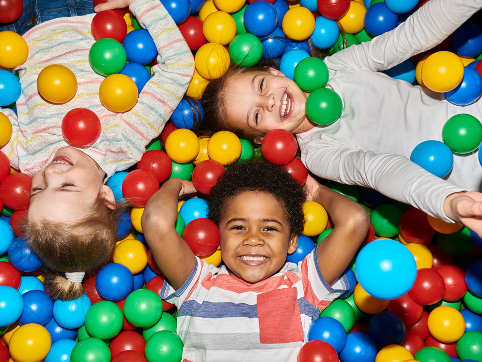 Photograph of three children laying in a multi-colored ballpit.