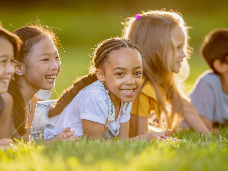 Photograph of several children smiling away from the camera with one kid smiling at the camera at golden hour. 