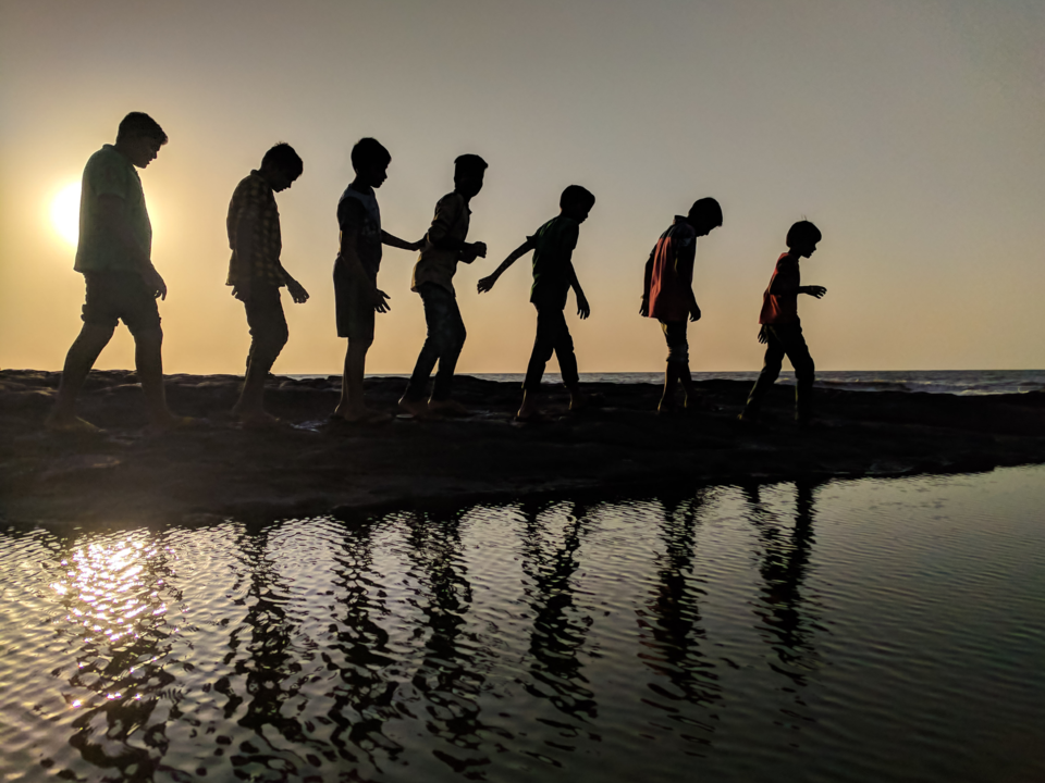 Group of kids walking along the beach at sunset.
