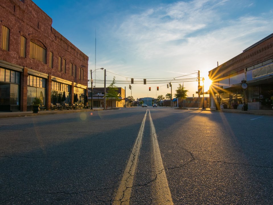 Photograph of an empty road in a town with the sun shining on a partly cloudy day.