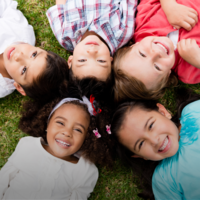Photograph of five children laying on the grass smiling at the camera.
