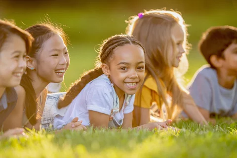 Photograph of several children smiling away from the camera with one kid smiling at the camera at golden hour. 