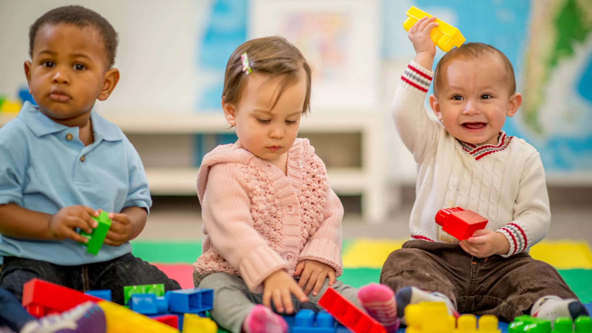 Photograph of three children playing with large lego blocks in a preschool